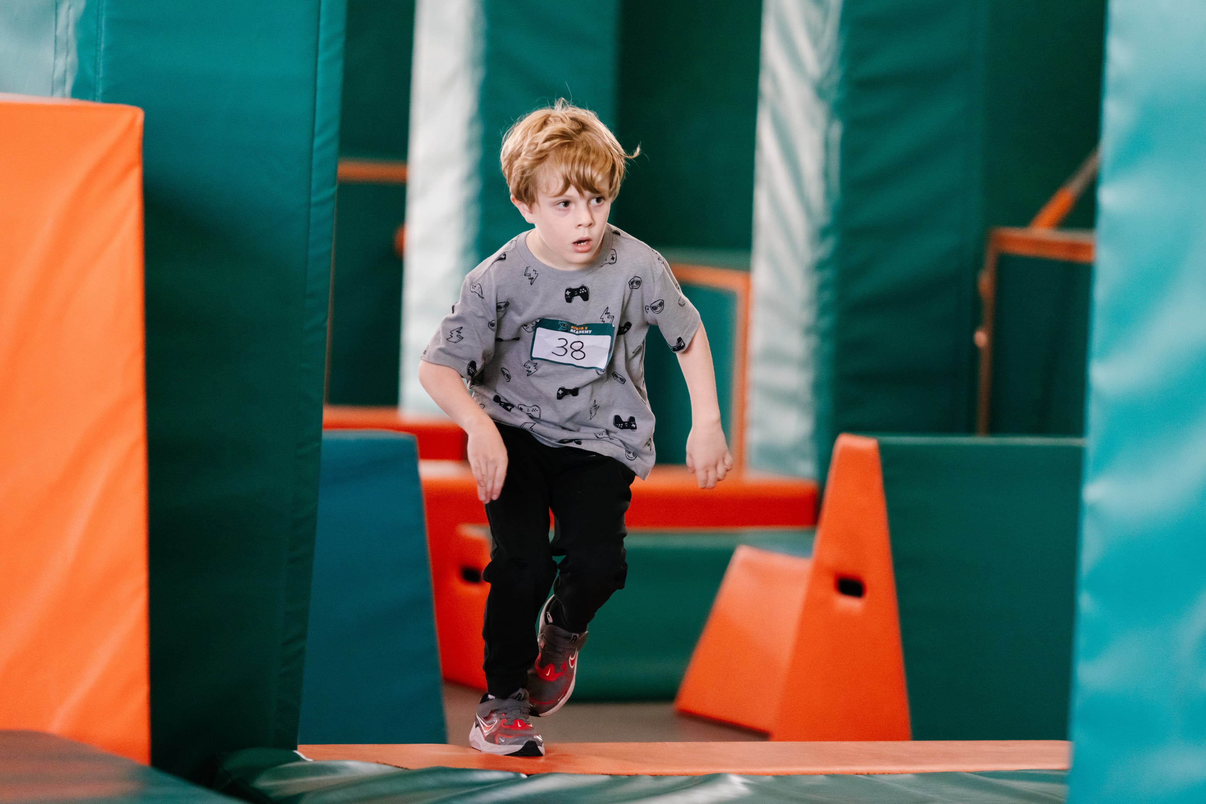 A young competitor with race bib 38 running through the padded obstacle course