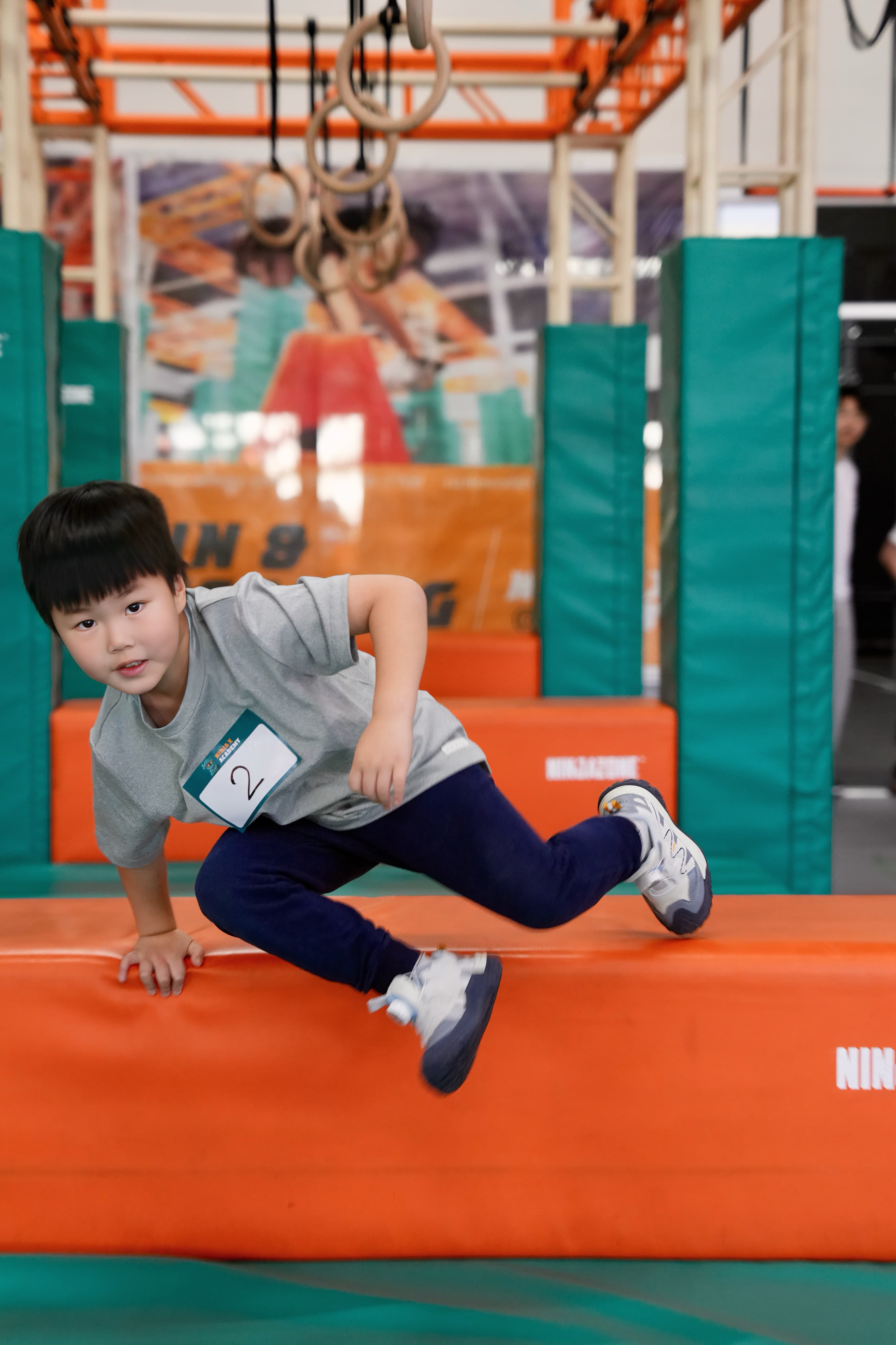 A small child vaulting over a padded orange obstacle in the Ninja X gym