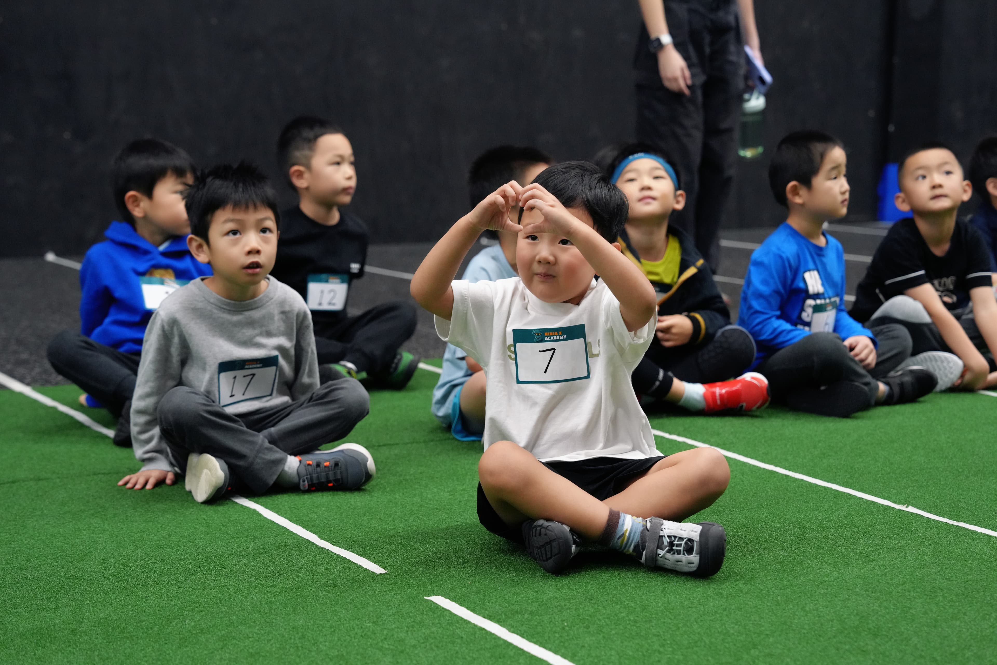 Young competitors sitting cross-legged on the turf watching the event